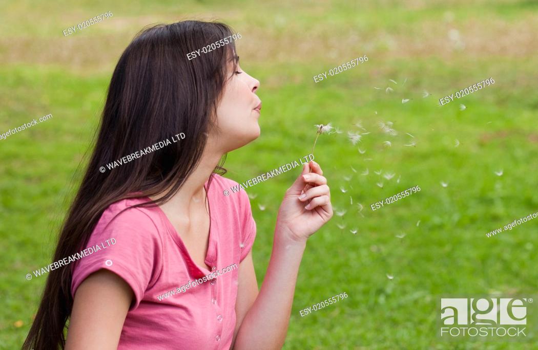 Stock Photo: Young woman standing up in a park while blowing a dandelion.