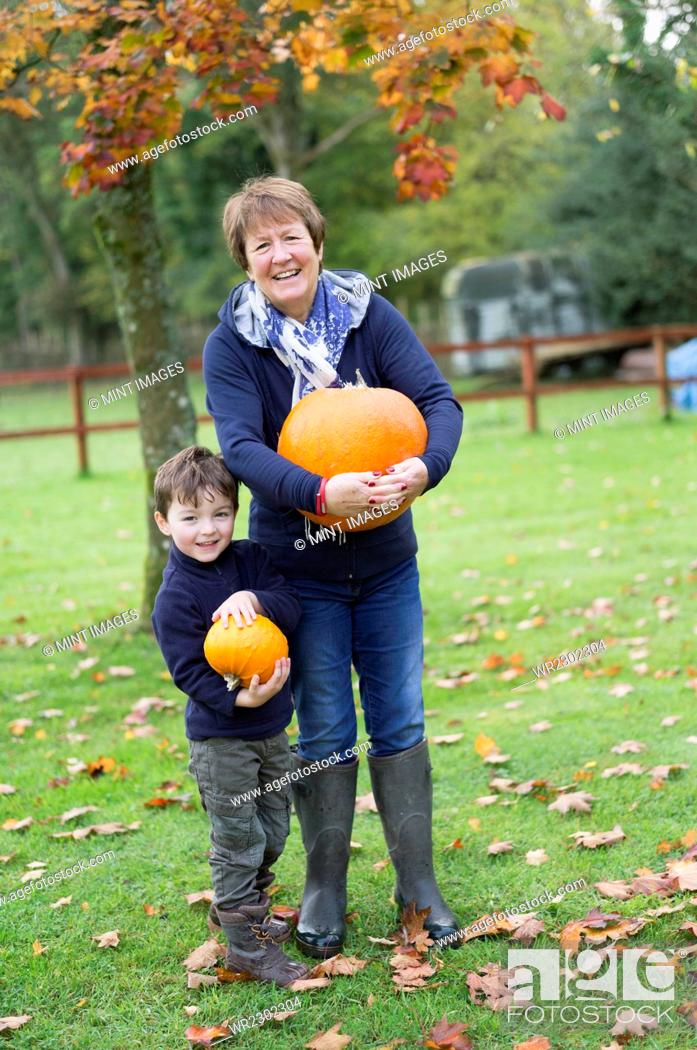 Stock Photo: A mature woman and a small boy holding pumpkins, large and small.