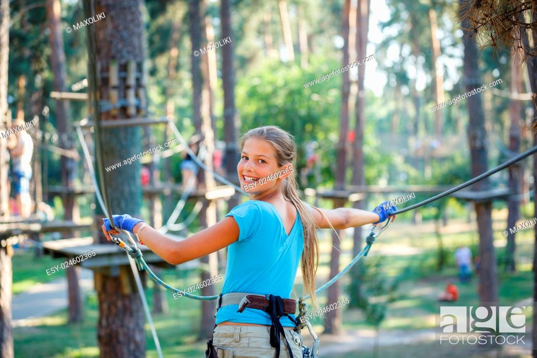 Stock Photo: Happy school girl enjoying activity in a climbing adventure park on a summer day.