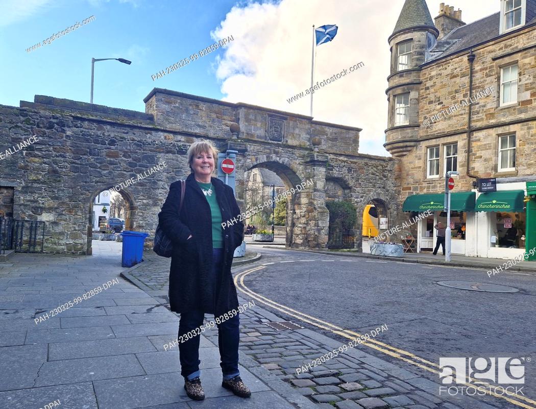 Stock Photo: 24 March 2023, Great Britain, St. Andrews: Independence activist Jane Philips from Dundee stands in front of an archway and a Scottish flag in the Scottish town.