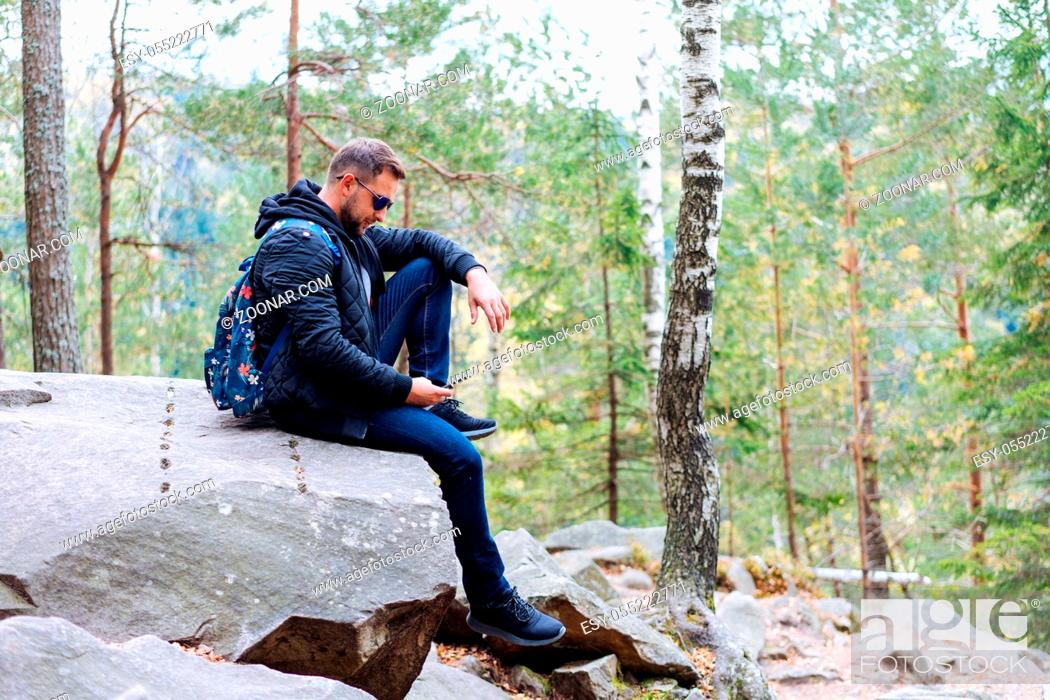 Stock Photo: guy sits in the woods on a rock and makes a selfie.