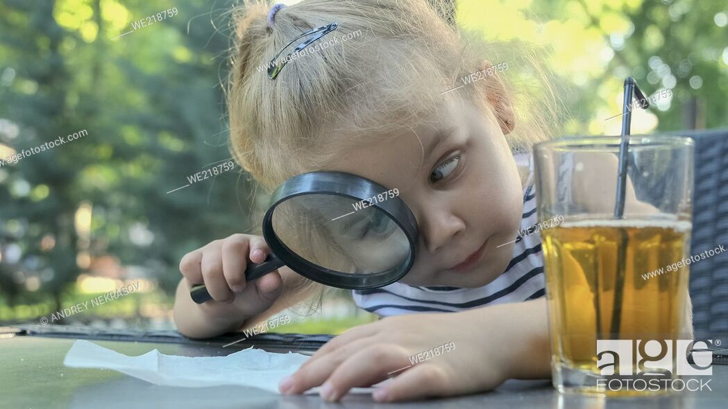 Stock Photo: Little girl carefully looks into the lens at the salt. Close-up of blonde girl is studying salt crystals while looking at her through magnifying glass while.
