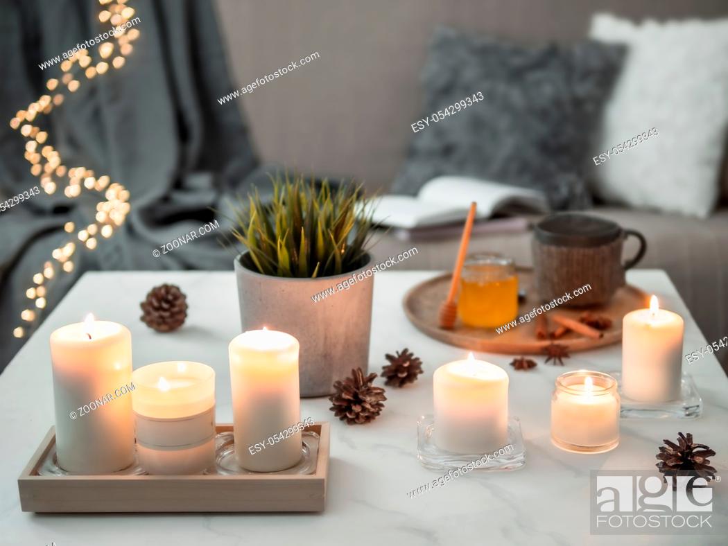 Stock Photo: Cozy home, hygge, cosiness concept - burning white fragrance candles on white marble table near sofa with pillows and plaid.