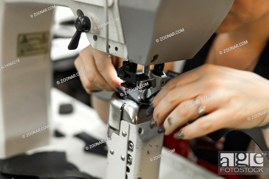 Imagen: Sewing machine in a leather workshop in action with hands working on a leather details for shoes. Women's hands with sewing machine at shoes factory.