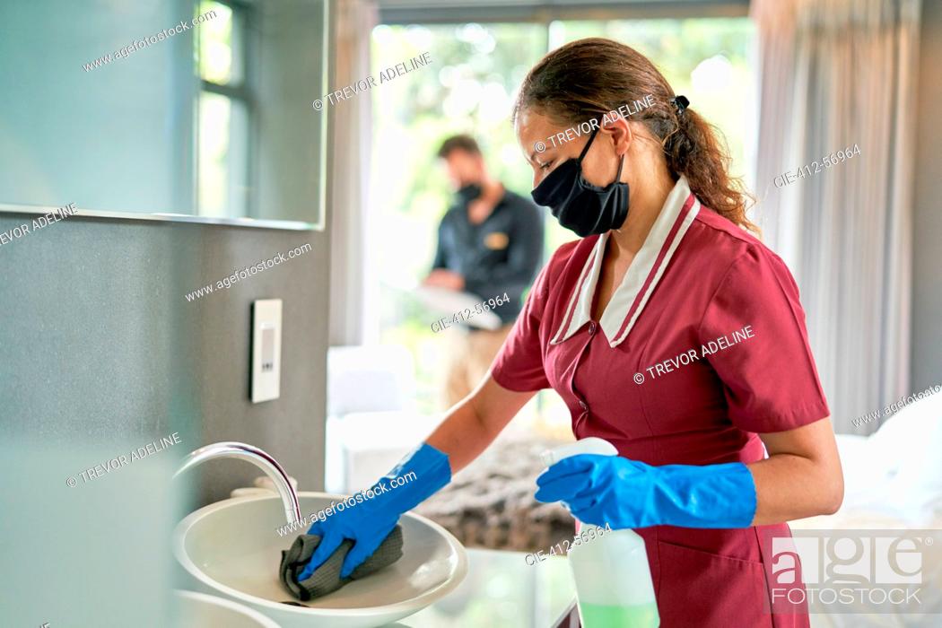 Stock Photo: Female hotel maid in face mask and gloves cleaning hotel room bathroom.