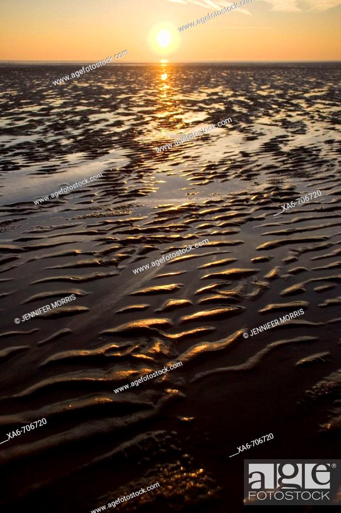Stock Photo: Sunset at the English coast, the weat sand in the foreground is touched with gold and the sun hovers just above the horizon.