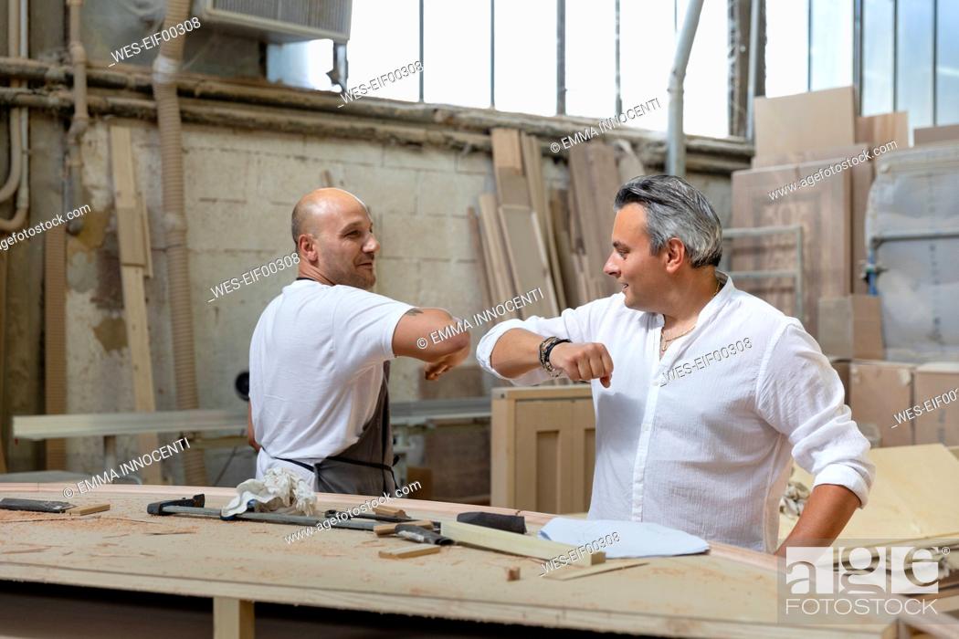 Stock Photo: Project manager and coworker giving elbow bump while standing in factory.