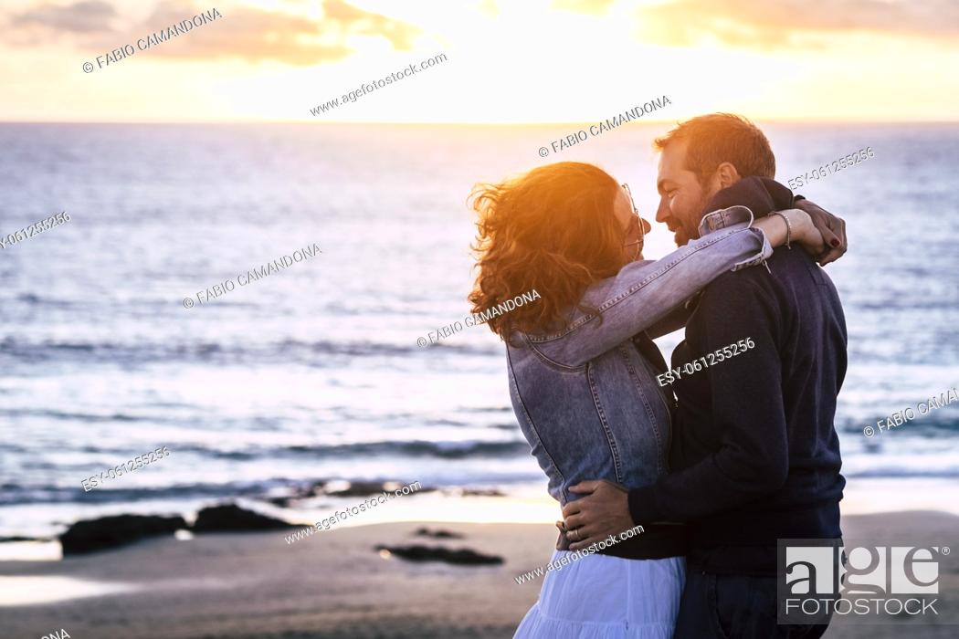 Photo de stock: Romantic mature couple in love kissing outdoor against an amazing sunset at the beach with ocean background. Relationship with man and woman hugging outdoors.
