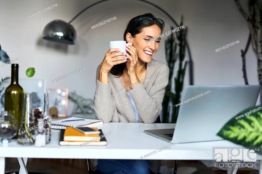 Stock Photo: Happy young woman at home with laptop on desk.