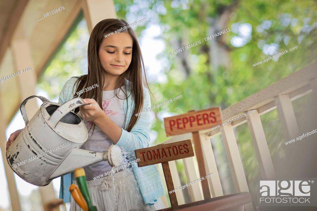 Stock Photo: A child holding a watering can, watering a a pot with newly planted tomato and pepper seeds.