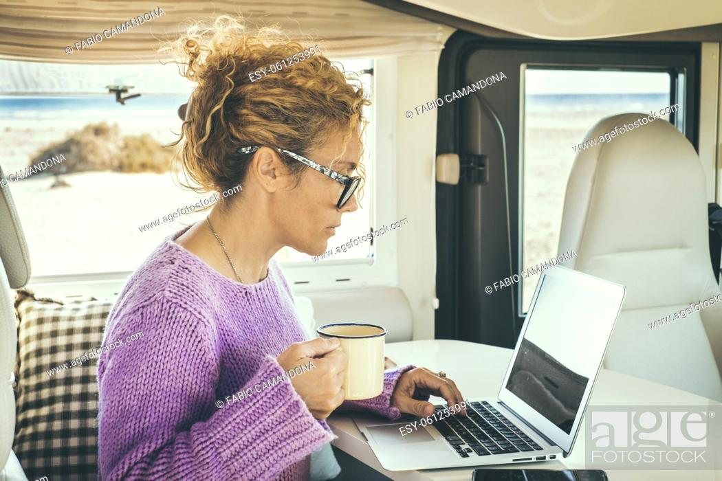 Stock Photo: Adult woman use laptop sitting inside a camper van. Concept of digital nomad lifestyle and wireless internet connection during travel.