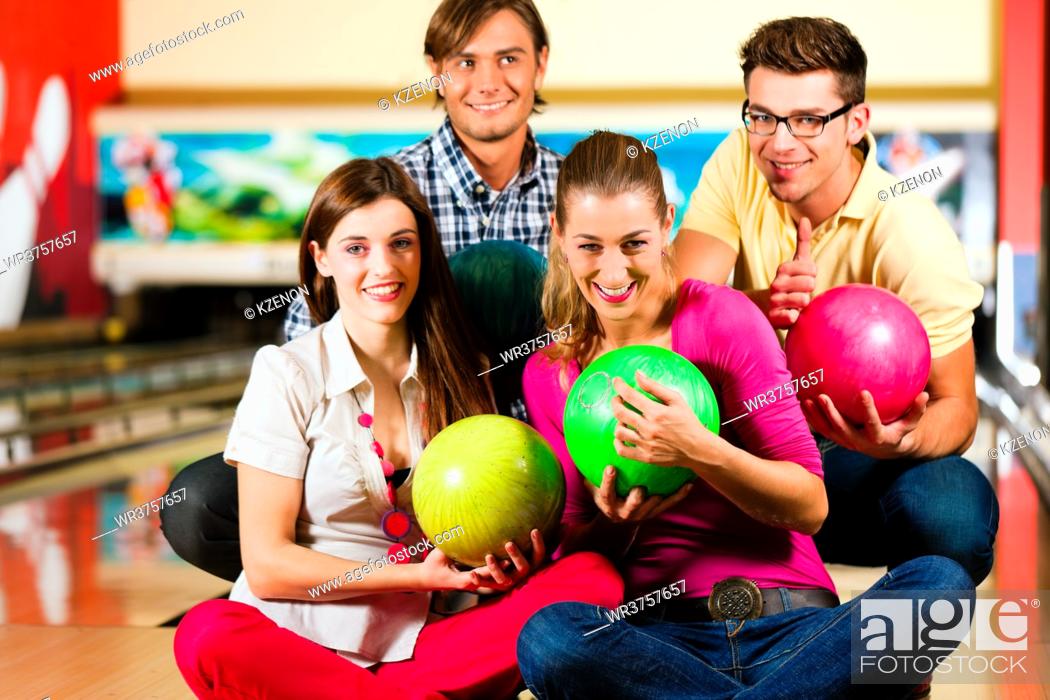 Imagen: Group of four friends in a bowling alley having fun, holding their bowling balls.