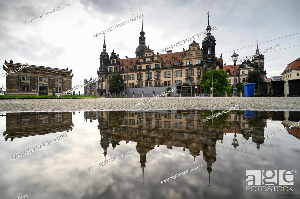 Stock Photo: 27 September 2021, Saxony, Dresden: The Schinkelwache (l-r), the Residenzschloss and rubbish bins placed on the footpath are reflected in a puddle in the.