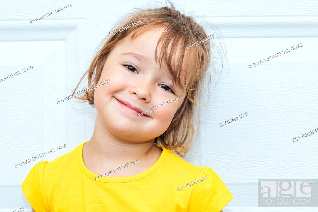 Stock Photo: Adorable blond-haired girl wearing a yellow shirt leaning against white background.