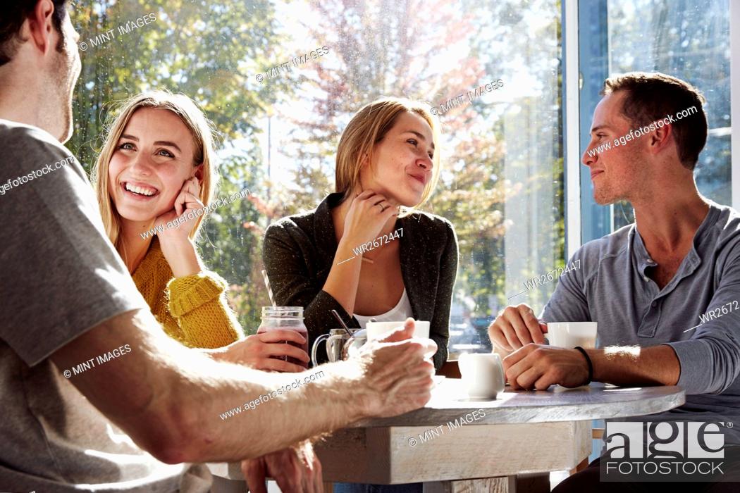 Stock Photo: Four people sitting at a table talking, with mugs and jars of smoothies.