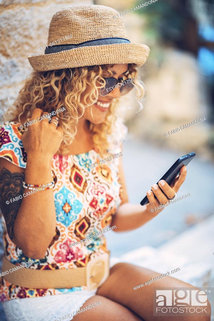 Stock Photo: Beautiful smiling hipster young woman in sunglasses and straw hat feeling excited on receiving good news using mobile phone while sitting outdoors.