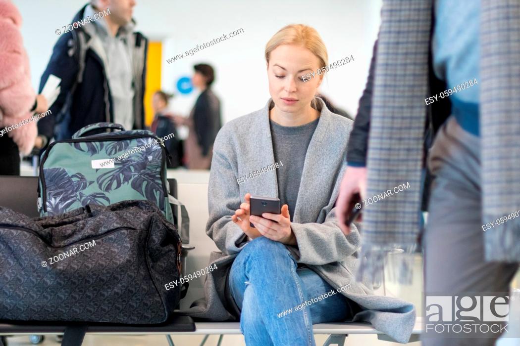 Imagen: Casual blond young woman using her cell phone while waiting to board a plane at the departure gates at the airport terminal.
