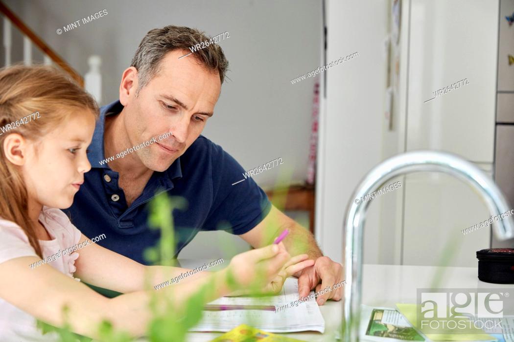 Stock Photo: A young girl and her father sitting looking at her school books, doing her homework.