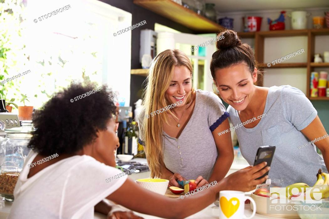 Stock Photo: Female Friends Making Breakfast Whilst Checking Mobile Phone.