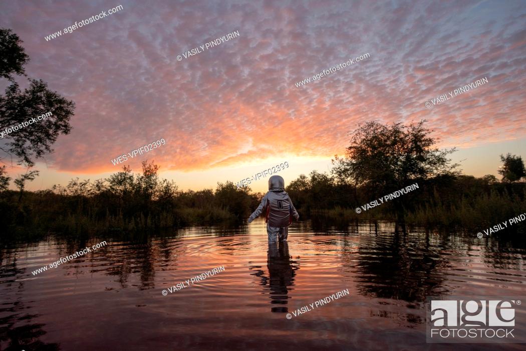 Stock Photo: Spacewoman walking in water at sunset.