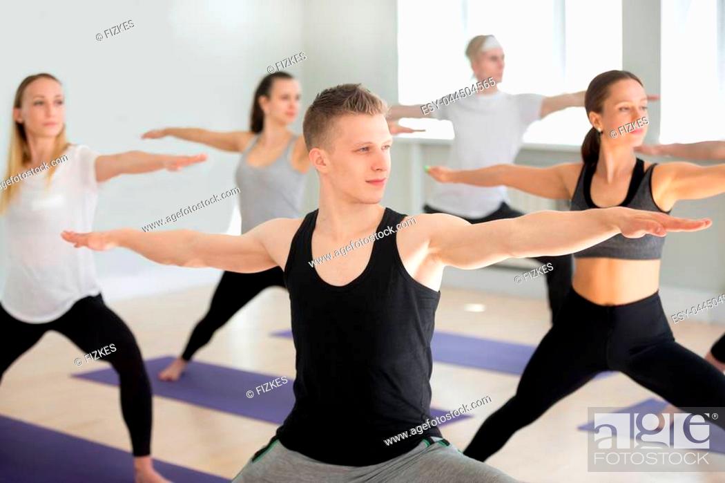 Stock Photo: Group of young sporty people practicing yoga lesson, doing Warrior exercise, Virabhadrasana 2 pose, working out, indoor close up.