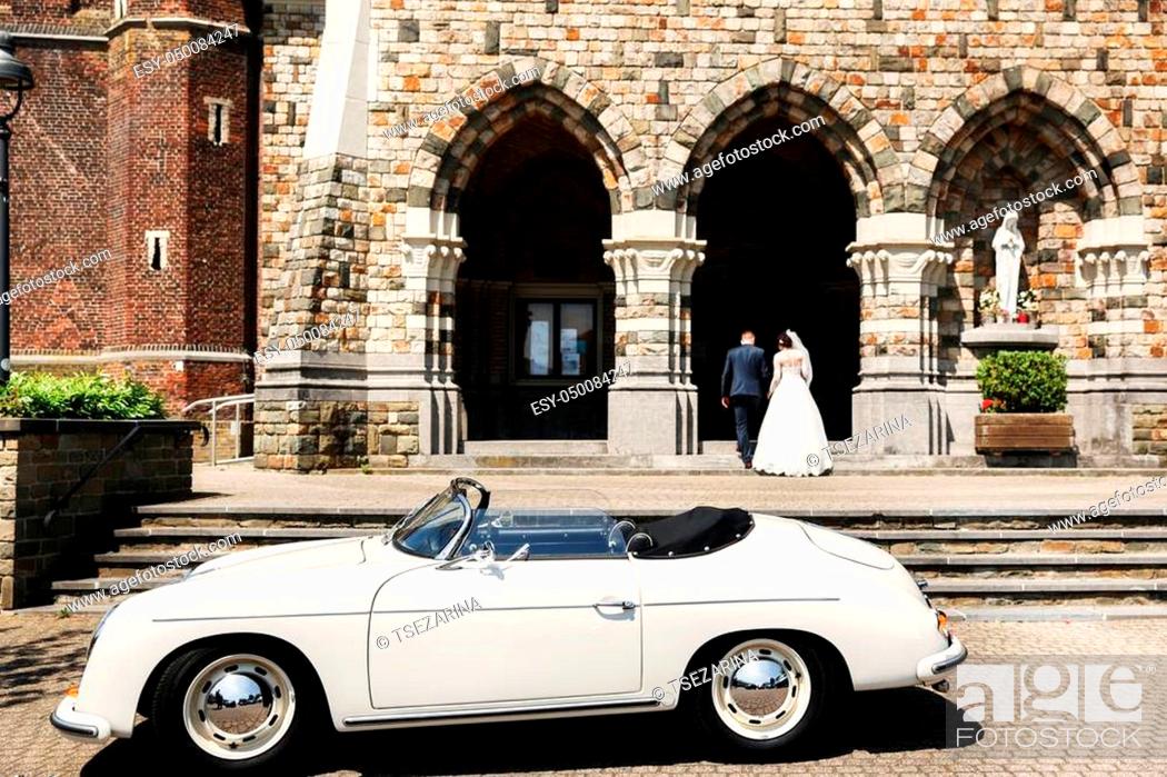 Stock Photo: Newlyweds are walking up the stairs of the church and old white car.