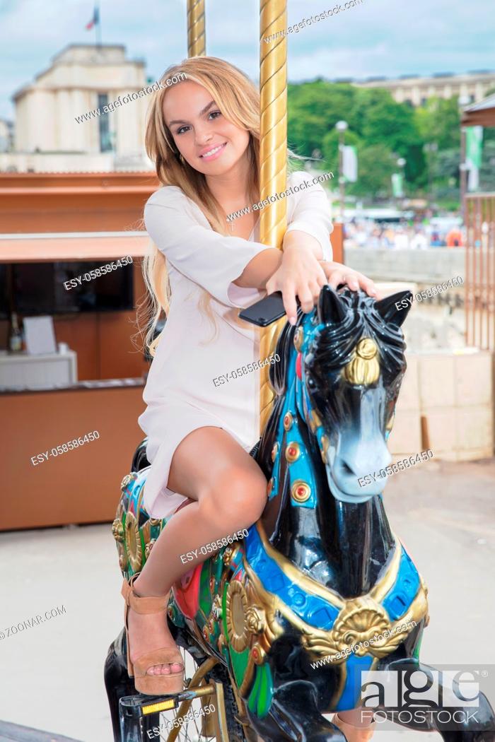 Stock Photo: Charming woman posing sitting on a carousel horse wearing a dress.