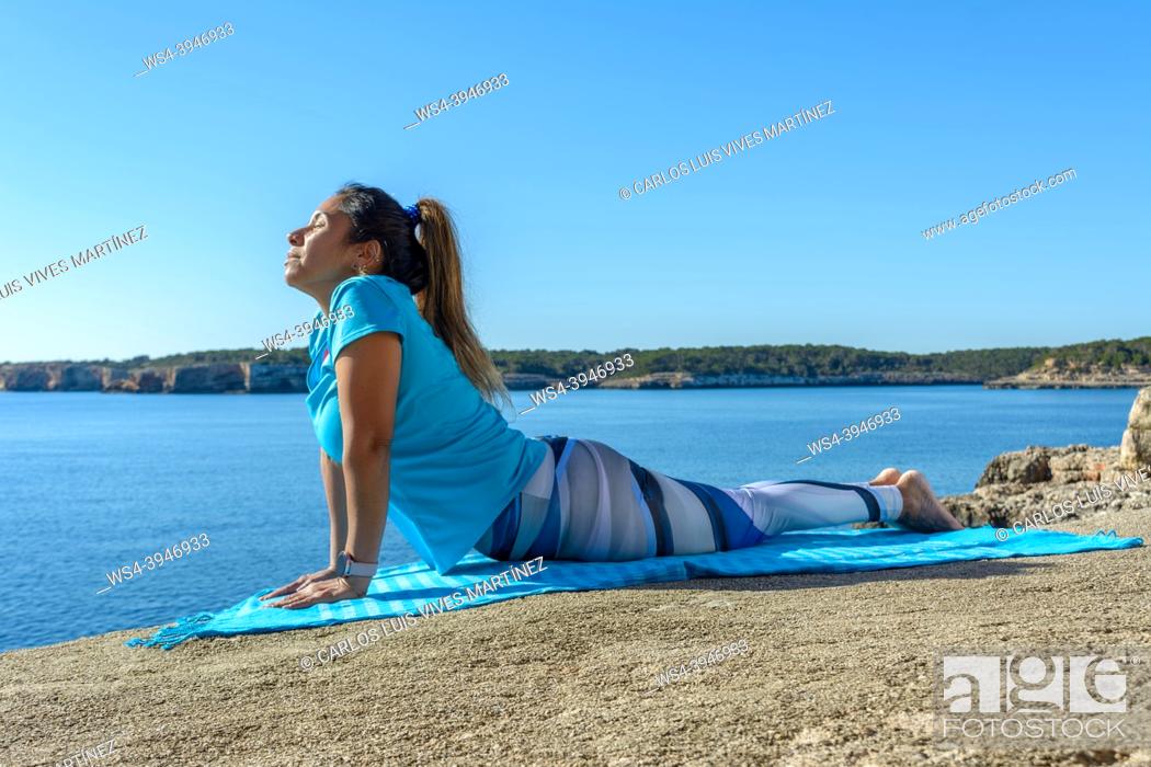 Imagen: middle-aged fitness woman outdoors in front of the sea does yoga stretching exercises.