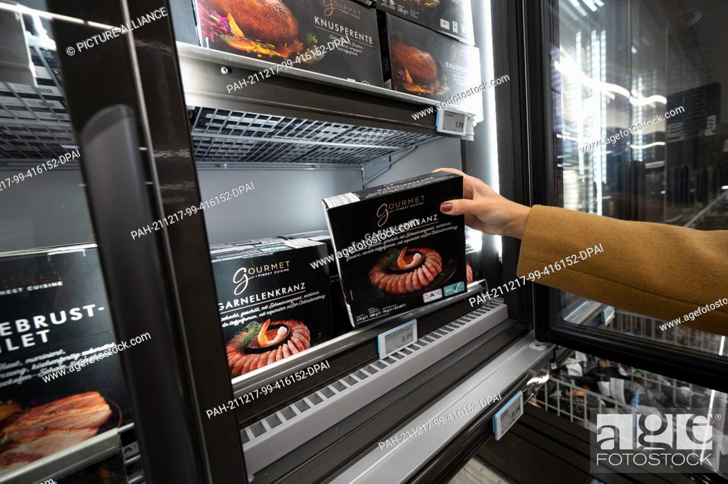 Stock Photo: PRODUCTION - 14 December 2021, North Rhine-Westphalia, Mülheim an der Ruhr: A woman takes a pack of shrimp out of the freezer at an Aldi store.