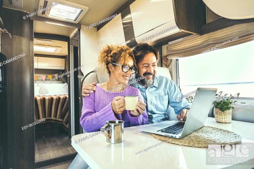 Photo de stock: Modern couple use together laptop inside camper van. Computer leisure people surfing the web. Traveler planning next destination smiling and enjoying freedom.