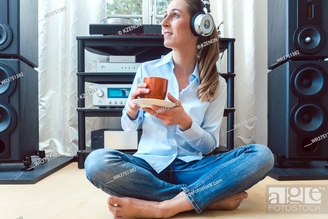 Stock Photo: Woman drinking coffee and listening to music sitting on the floor of her home.