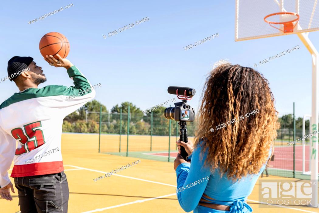 Stock Photo: Female filming male friend playing basketball on sports court.