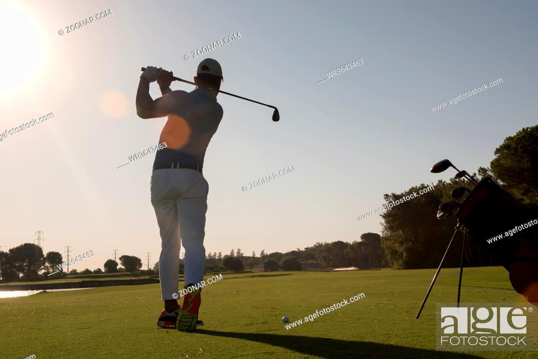 Stock Photo: golf player hitting shot with club on course at beautiful morning with sun flare in background.