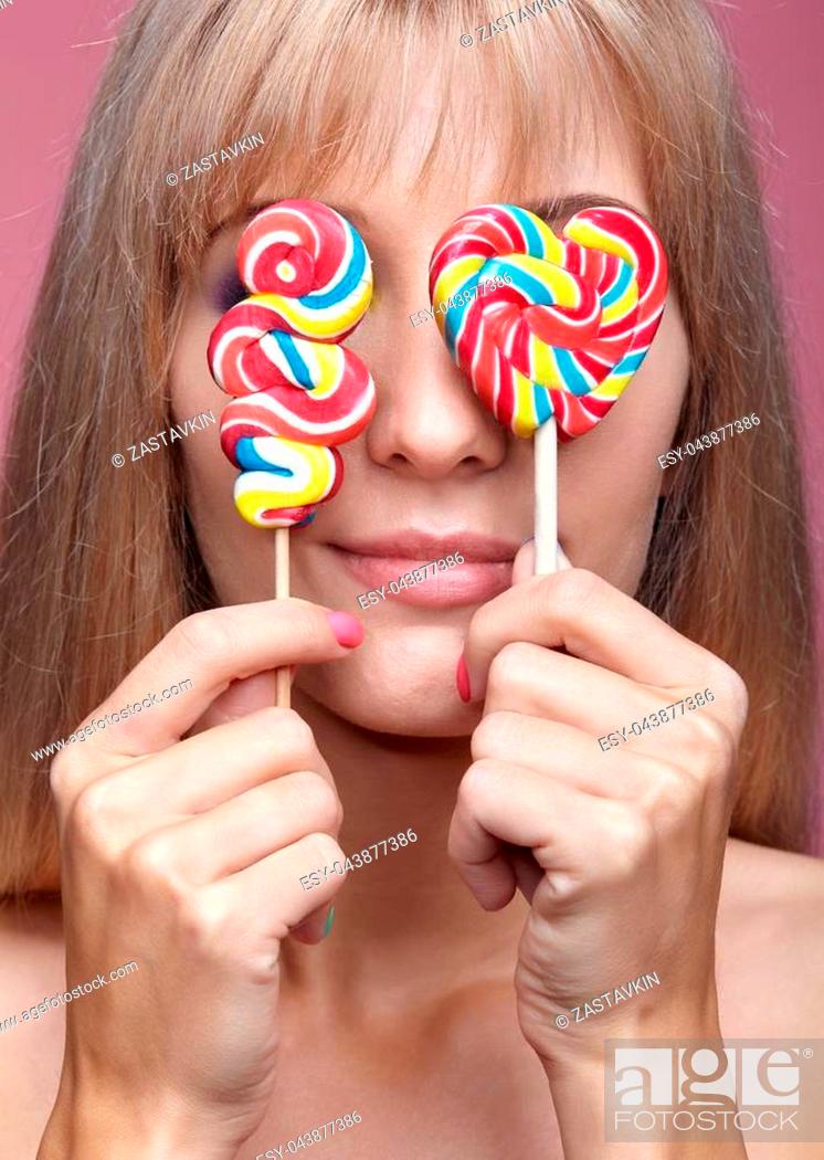Photo de stock: Beauty portrait of young blonde woman on pink background. Female with candy lollipop on stick in hands. Girl has finger nails with bright yellow, green.