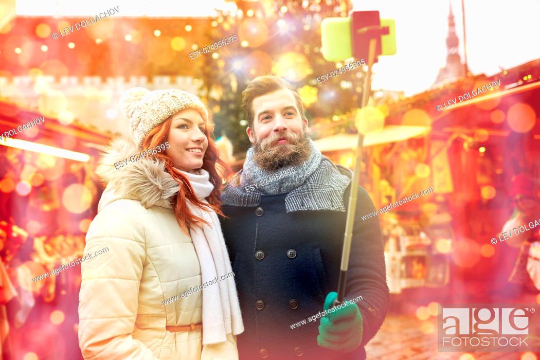 Stock Photo: holidays, winter, christmas, technology and people concept - happy couple of tourists in warm clothes taking picture with smartphone selfie stick in old town.