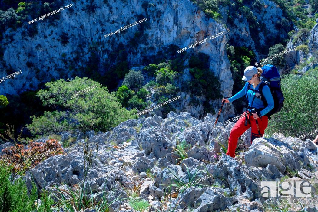 Stock Photo: A young woman with trekking gear hiking through the mountainous coastal landscape, Selvaggio Blu, Sardinia, Italy, Europe.