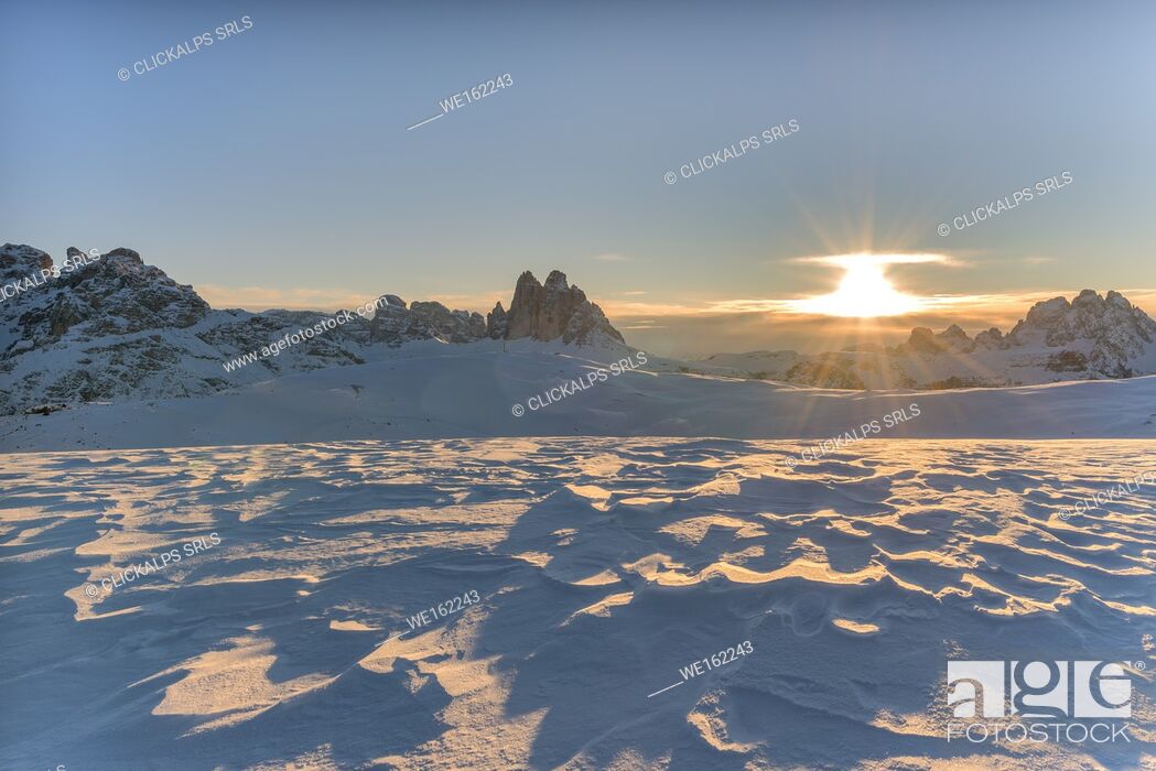 Stock Photo: Prato Piazza/Plätzwiese, Dolomites, province of Bolzano, South Tyrol, Italy. Patterns in wind-eroded snow. In the background the rising sun and the famous peaks.