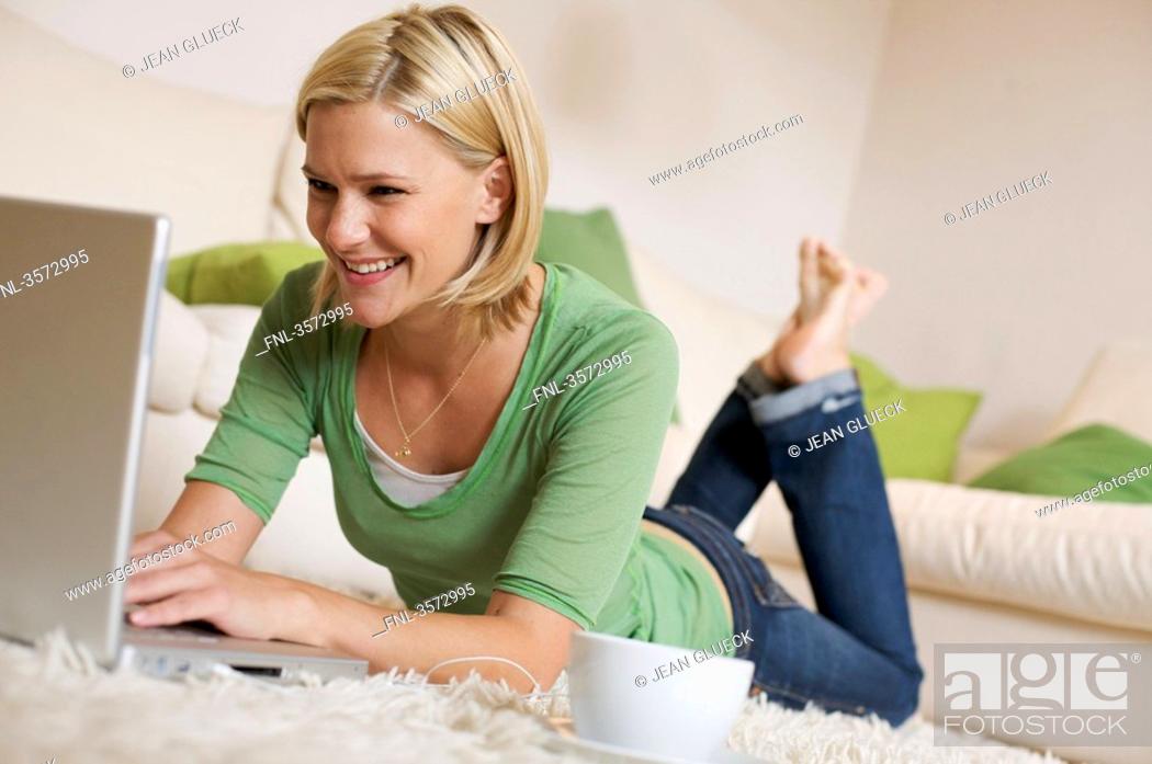 Stock Photo: Young woman lying on rug with cup of coffee, earbuds and laptop.