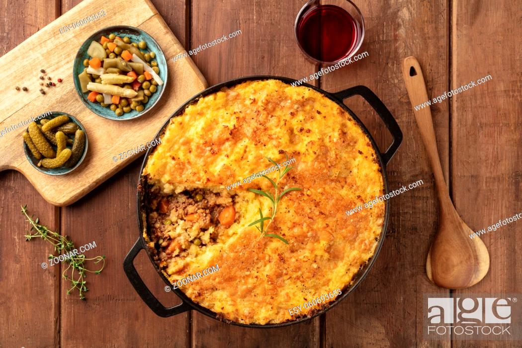 Stock Photo: Shepherd's pie with pickles, herbs, and red wine, shot from above on a dark rustic wooden background.