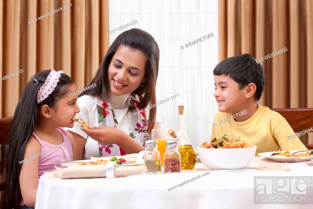 Stock Photo: Cheerful mother feeding her daughter pizza with son sitting besides.