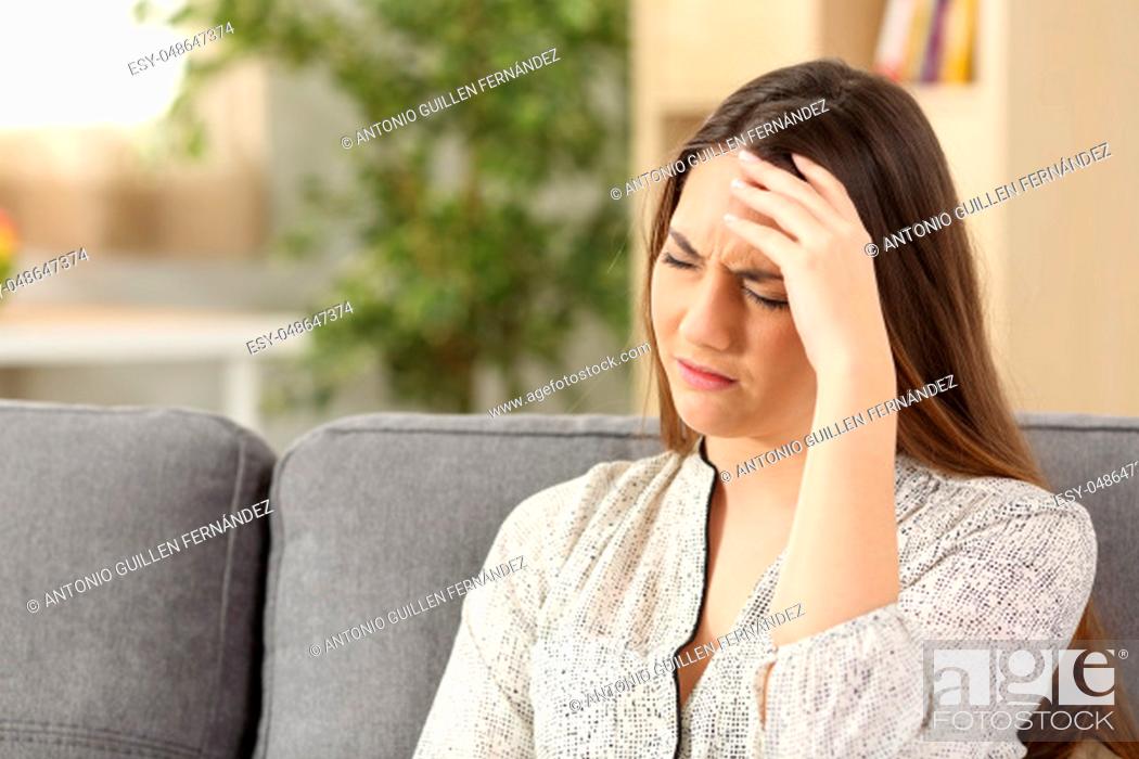 Stock Photo: Lady suffering head ache sitting on a sofa in the living room at home.