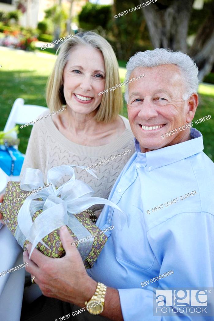 Stock Photo: Middle-aged Couple sitting Holding a Gift outside.