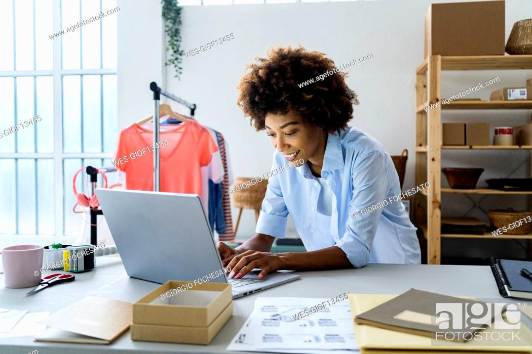 Stock Photo: Young female fashion designer using laptop while leaning on desk at studio.