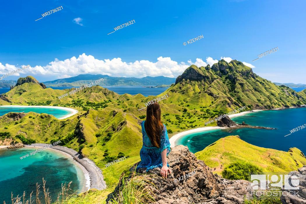 Stock Photo: Rear view of a young woman enjoying the awesome view of Padar Island, while sitting on the top of a volcanic mountain during summer vacation in Indonesia.