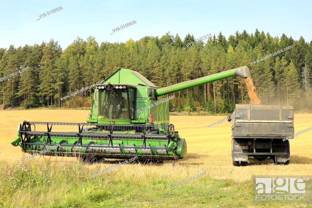 Stock Photo: Salo, Finland - September 8, 2018: John Deere combine unloads harvested grain onto truck trailer on a clear day of autumn in South of Finland.