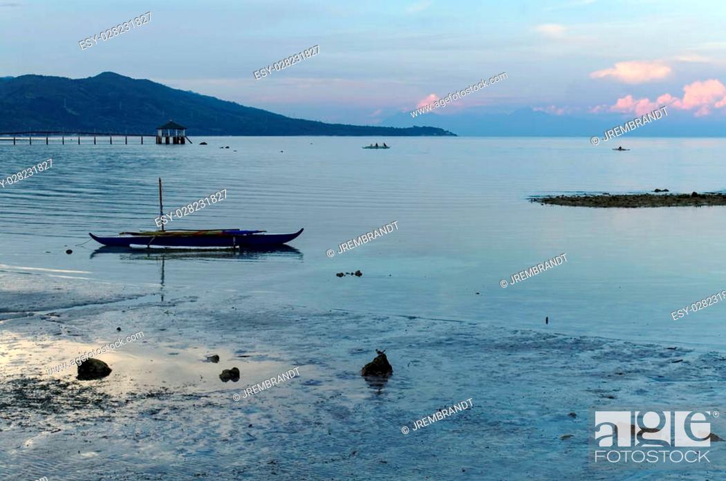 Stock Photo: A Blue Morning At the Beach. There are a few people around, boats are left on the shore, and the water has receded outwards.