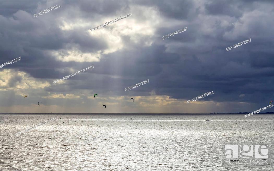 Stock Photo: dramatic illuminated coastal scenery including some kitesurfers near Neuharlingersiel in Eastern Frisia, Germany.