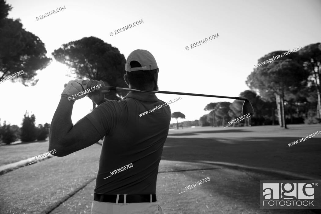 Photo de stock: golf player hitting shot with club on course at beautiful morning with sun flare in background.