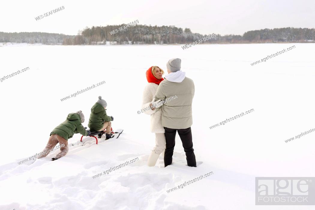 Stock Photo: Couple embracing each other by sons tobogganing on snow in winter.