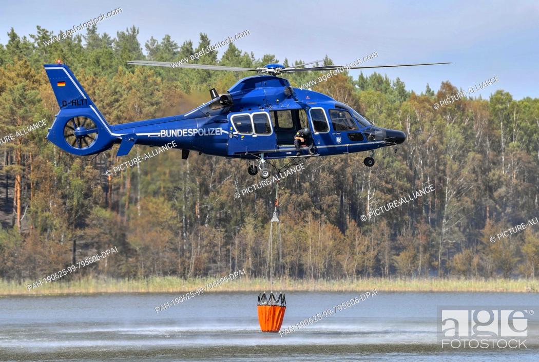 Stock Photo: 25 June 2019, Brandenburg, Lieberose: A helicopter of the federal police picks up water in the tar furnace lake to fight the forest fire in the Lieberoser Heide.